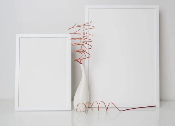 在白色桌子上和墙上的现代白色花瓶里 有两个用干枯的绳子装饰的模拟的白色木制海报框架 — 图库照片