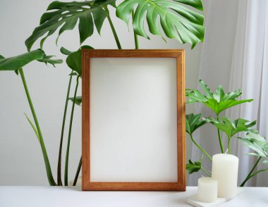 Kahverengi poster çerçevesi, filizotu yeşili yaprak ve aroma beyaz mumlar bej masa ve duvar arkaplanı, beyaz yumuşak iç ses tonu