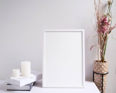 Beyaz poster çerçevesi, mumlar, kitap ve güzel kurumuş çiçekleri modern ahşap vazo kompozisyonu ile beyaz ahşap masa odasının iç kısmı üzerine yerleştirin. 