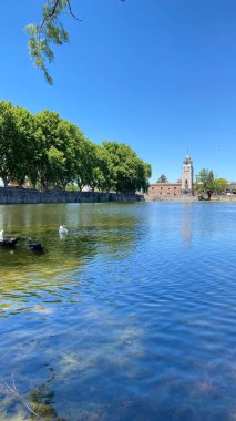 Önünde ördekler yüzen Tajamar rezervuarının huzurlu manzarası ve parlak mavi gökyüzünün altında ikonik El Tajamar saat kulesi.