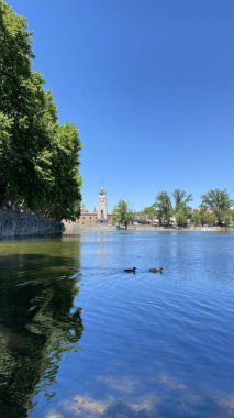 Önünde ördekler yüzen Tajamar rezervuarının huzurlu manzarası ve parlak mavi gökyüzünün altında ikonik El Tajamar saat kulesi.