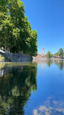 Önünde ördekler yüzen Tajamar rezervuarının huzurlu manzarası ve parlak mavi gökyüzünün altında ikonik El Tajamar saat kulesi.