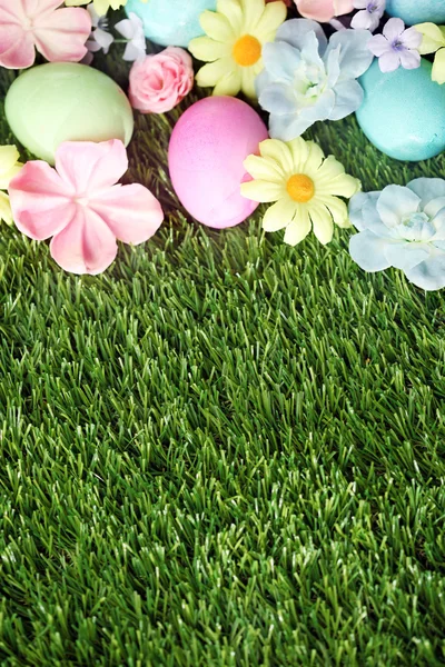 Telur Paskah berwarna di rumput dengan bunga latar belakang — Stok Foto