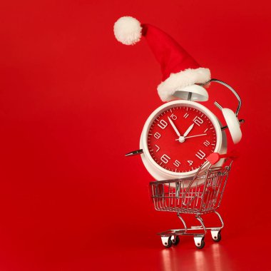 Noel Baba şapkası kırmızı saat üzerinde, alışveriş arabasında dengelenmiş. Mesaj için boş alanı olan son dakika Noel alışverişi kavramı.