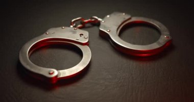 Suçluları tutuklamak için kolluk kuvvetleri tarafından kullanılan bir çift kelepçe. Kırmızı ve mavi yanıp sönen polis ışıklarıyla. Adalet ya da suçlu bir kavramı yakalamak.