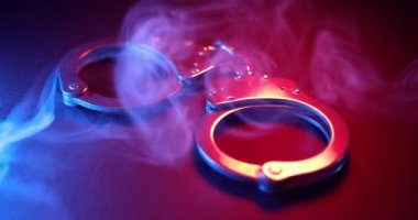 Suçluları tutuklamak için kolluk kuvvetleri tarafından kullanılan bir çift kelepçe, kırmızı ve mavi ışıklarla aydınlatılmış. Adalet ya da suçlu bir kavramı yakalamak.