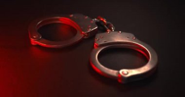 Suçluları tutuklamak için kolluk kuvvetleri tarafından kullanılan bir çift kelepçe. Kırmızı ve mavi yanıp sönen polis ışıklarıyla. Adalet ya da suçlu bir kavramı yakalamak.