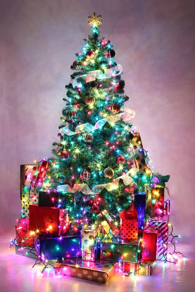 Geschmückter Weihnachtsbaum mit bunten Lichtern, umgeben von Pre — Stockfoto