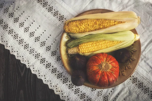 Autumn still life in rustic style flat lay with pumpkin , corn,  and figs on a white tablecloth with lace