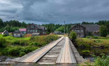 31 Temmuz 2021 Karelia Rusya 'nın tarihi Pyalma köyü, eski ahşap evler, nehir üzerinde bir köprü. 