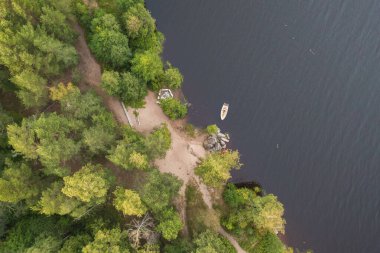 Orman kıyısının yanındaki nehirde bir tekne. Üst İHA görünümü