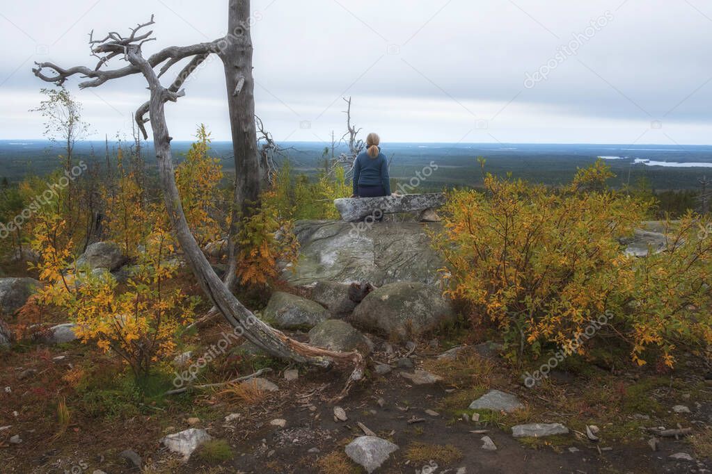 woman sitting on mystical mountain Vottovaara in Karelia during the golden autumn. Russian northern landscape  