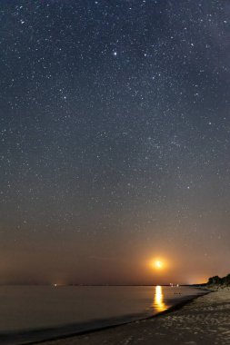 Gece yıldızlı gökyüzü ve deniz sahilinde yükselen ay.