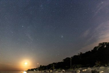 Gece yıldızlı gökyüzü ve deniz sahilinde yükselen ay.