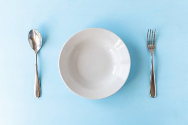 Açık mavi arkaplanda boş tabak, kaşık ve çatal