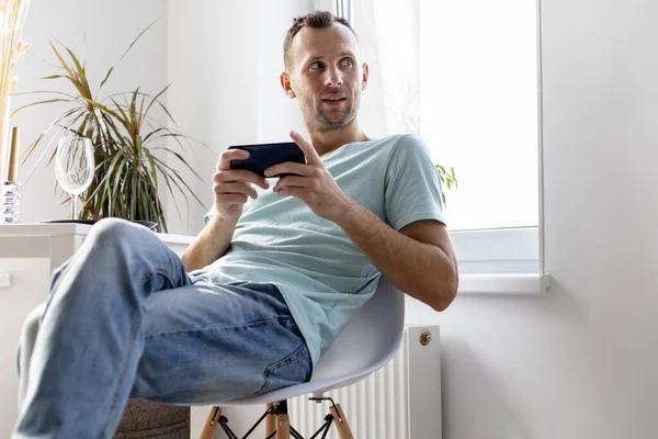 Jovem Shirt Jeans Senta Uma Cadeira Quarto Brilhante Com Smartphone Fotografia De Stock