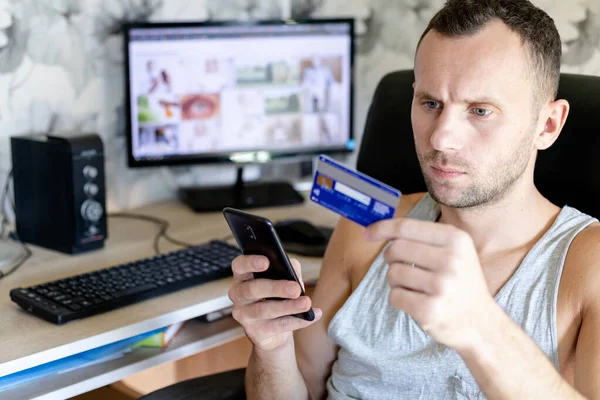 Ernster Mann Sitzt Einem Computertisch Mit Kreditkarte Und Smartphone Der lizenzfreie Stockbilder