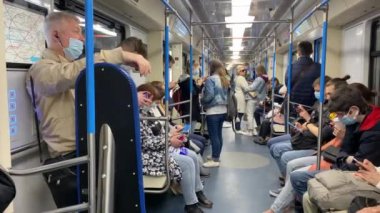 Metrodaki insanlar maske takıp aletlerine bakıyorlar..