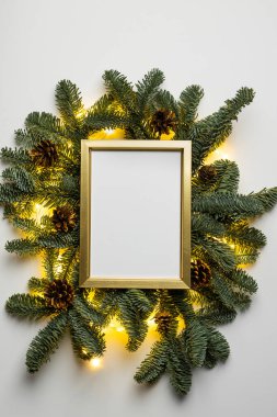 Beyaz arka planda köknar dalları, koniler ve ışıklardan oluşan boş altın bir sınır