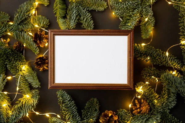 Siyah arka planda köknar dalları, koni ve ışıklardan oluşan boş kahverengi ahşap bir sınır.