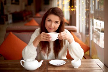 Genç kadın kafede çay içiyor. Çay için beyaz çaydanlık, şeker kasesi ve fincanlı masa hazır. Sabah oldu.