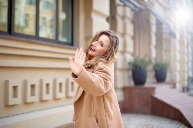 Kadın şehrin caddesinde yürüyor ve el sallıyor ya da merhaba diyor. Kadın el hareketi selamlama ya da güle güle
