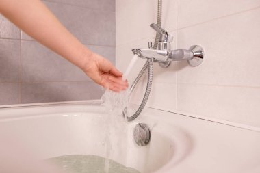 Kadın evde banyo yapıyor, sıcaklığı kontrol ediyor, suya elle dokunuyor. Sıcak suyun altındaki parmaklar lavabonun musluğundan ya da banyo küvetinden.