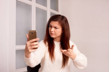 Canı sıkkın kadın, gri arka planda akıllı telefonun çektiği hataları açıklıyor.