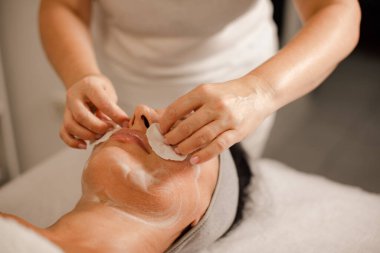 Masöz kadın yüz masajından önce müşterinin yüzünü temizliyor.