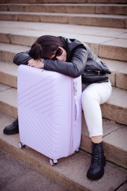 Merdivenlerde oturan yorgun kadın, kocaman bavuluyla.