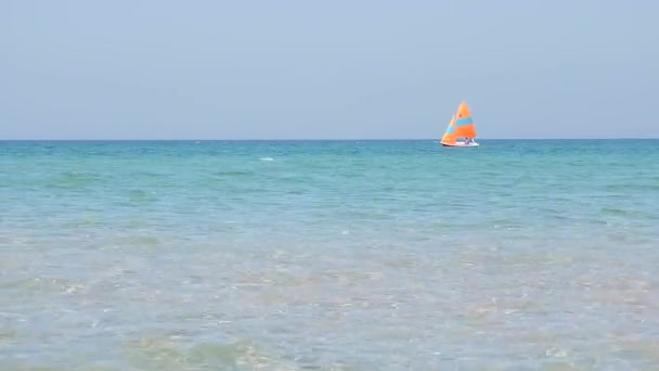 Een eenzame witte boot met een oranje zeil drijft op de azuurblauwe zee, de oceaan. De wind blaast het zeil — Stockvideo