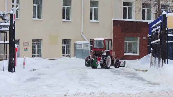 Трактор едет по улице и очищает дорогу от снега после сильного снегопада, метели — стоковое видео