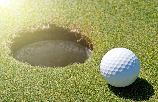 Bola de golfe ao lado de um buraco — Fotografia de Stock