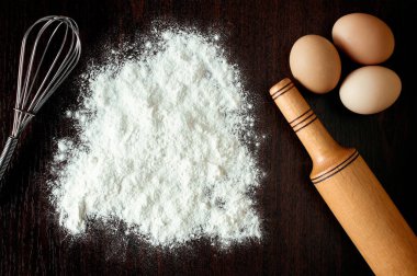 Buğdaylı un, yumurta, merdane, ahşap zemin üzerinde kaşık. Fırın ürünleri için malzemeler