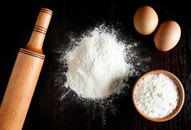 Buğdaylı un, yumurta, merdane, ahşap zemin üzerinde kaşık. Fırın ürünleri için malzemeler