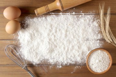 Buğdaylı un, yumurta, merdane, ahşap zemin üzerinde kaşık. Fırın ürünleri için malzemeler