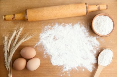 Buğdaylı un, yumurta, merdane, ahşap zemin üzerinde kaşık. Fırın ürünleri için malzemeler