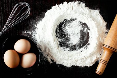 Buğdaylı un, yumurta, merdane, ahşap zemin üzerinde kaşık. Fırın ürünleri için malzemeler