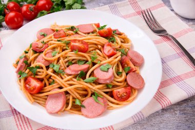 Kiraz domatesli makarna, kızarmış sosis ve beyaz tabakta maydanoz, nefis, doğal bir arka plan..