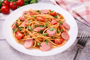 Kiraz domatesli makarna, kızarmış sosis ve beyaz tabakta maydanoz, nefis, doğal bir arka plan..