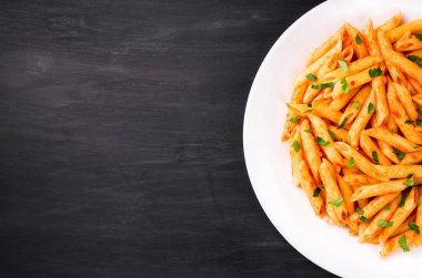 Domates soslu makarna, siyah arka planda maydanozla süslenmiş, çok lezzetli..