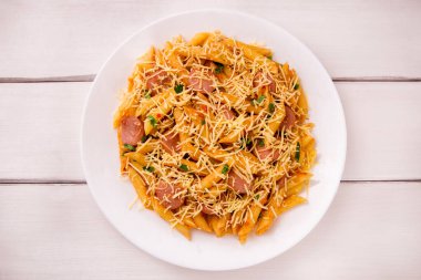 Sosis ve peynirli domates soslu makarna. Beyaz ahşap bir masada maydanozla süslenmiş. Çok lezzetli..