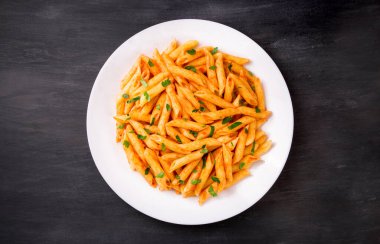 Domates soslu makarna, siyah arka planda maydanozla süslenmiş, çok lezzetli..