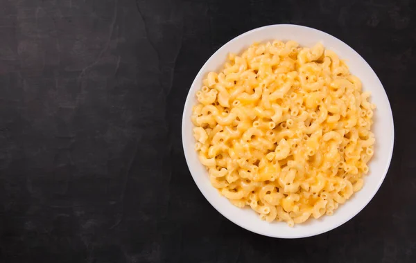 Macaroni and cheese on a white plate on a black background. American mac and cheese