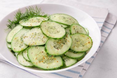 Beyaz arka planda baharatlar olan bir kasede salatalık salatası.