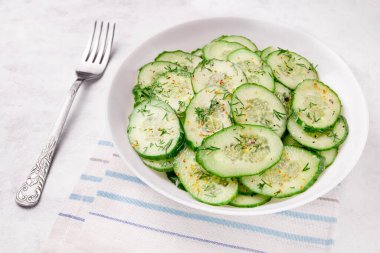 Beyaz arka planda baharatlar olan bir kasede salatalık salatası.