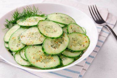 Beyaz arka planda baharatlar olan bir kasede salatalık salatası.