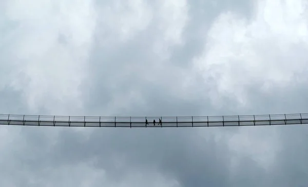 高悬索桥上的人的黑白照片 多云的天空 环状斑纹 — 图库照片