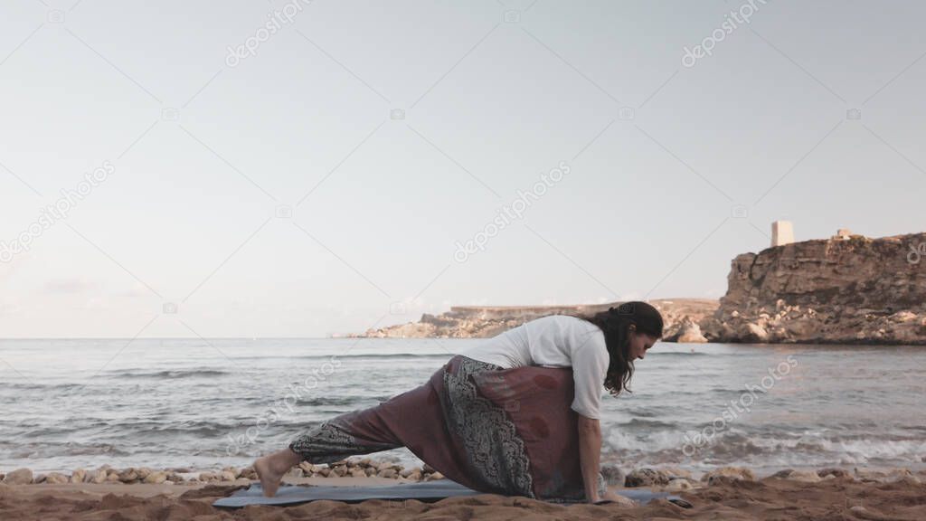 Young caucasian brunette woman doing youga on the sandy beach in the morning