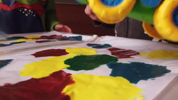 Artesanía infantil. Niños conduciendo camión de juguete en la parte superior de la carpeta de plástico con pintura — Vídeo de stock